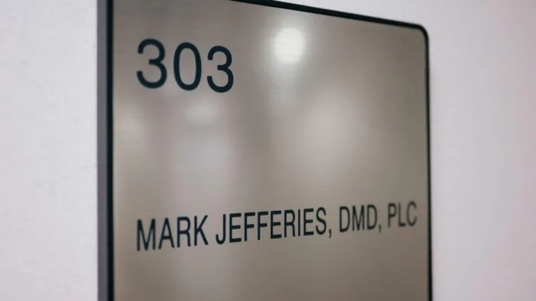 The image shows a metallic office sign mounted on a wall. The sign has the number "303" at the top and the name "MARK JEFFERIES, DMD, PLC" below it. This image is relevant as it indicates the office location and the name of the professional, likely a dentist, working in room 303.