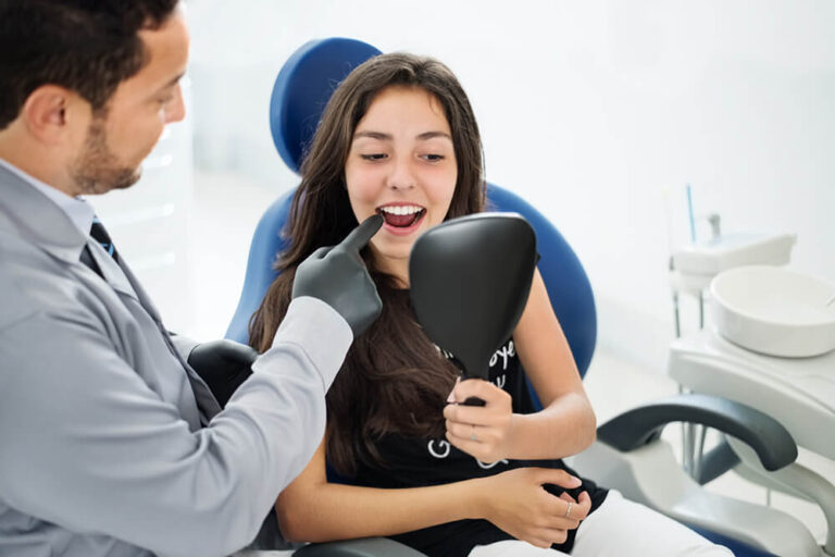 A patient handheld the mirror while sitting on a recliner dental chair while the dentist pointing something at her teeth, in a dental clinic.
