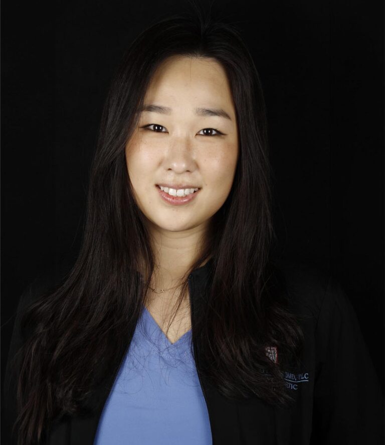 The image features a person wearing a blue shirt layered under a black jacket with text on the left side, possibly indicating a professional or medical affiliation.